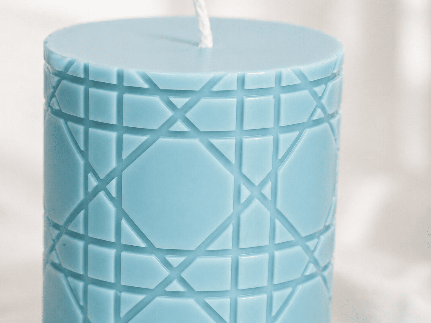 An extreme close-up view of a dusty blue pillar candle, focusing on the intricate geometric cannage pattern. Lines and edges are crisp, deep, and perfectly formed without imperfections.