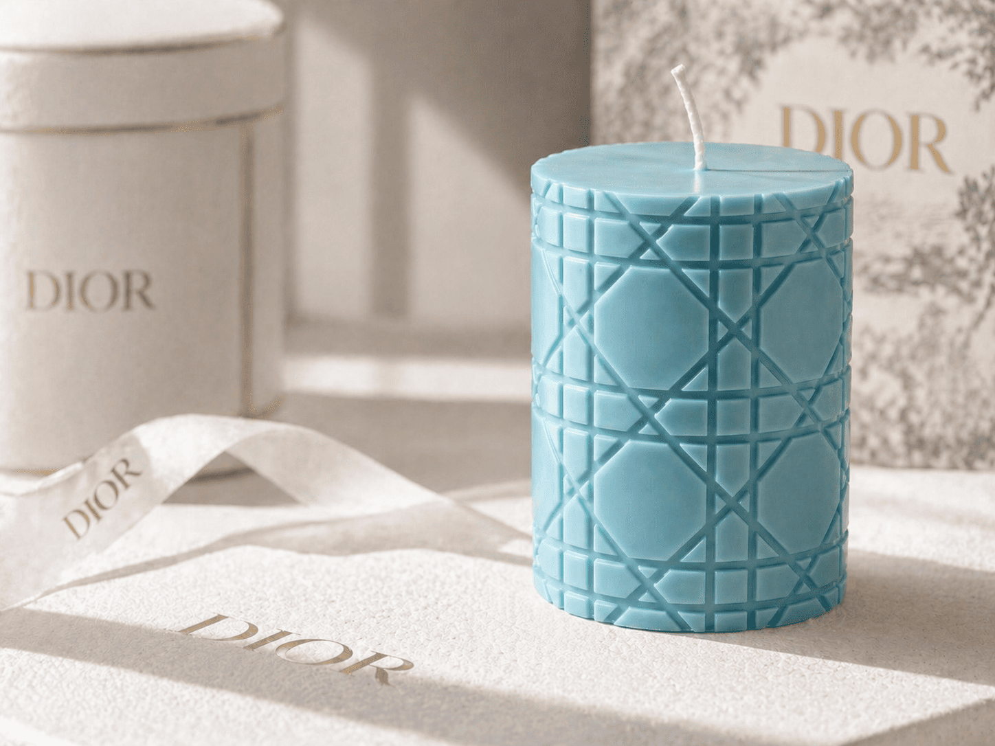 A finished dusty blue geometric woven pillar candle displayed in bright sunlight alongside premium custom branded packaging.